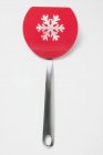 Gros plan vue de dessus de la spatule rouge avec perforation en forme de flocon de neige sur la surface blanche — Photo de stock