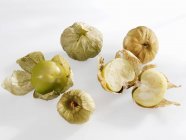 Several tomatillos, whole and halved  on white surface — Stock Photo