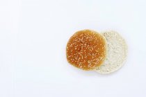 Draufsicht eines aufgeschnittenen Hamburgerbrötchens mit Sesam auf weißer Oberfläche — Stockfoto