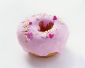 Vista de primer plano de una rosquilla esmerilada con glaseado rosa en la superficie blanca - foto de stock