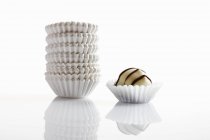 Closeup view of chocolate candy and paper cases on white surface — Stock Photo