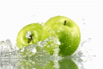 Два зеленых яблока с брызгами воды — стоковое фото