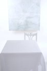 Ein leerer Tisch mit weißer Tischdecke, Stuhl und schäbigem Brett an der Wand — Stockfoto