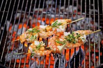 Closeup view of barbecued prawn skewers with herbs on grating over embers — Stock Photo