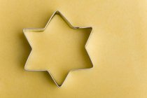 Vista close-up de cortador de biscoitos em forma de estrela na massa amarela — Fotografia de Stock