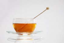 Vista de primer plano del té con palo de azúcar swizzle en taza de vidrio y platillo - foto de stock