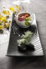 Vista de primer plano del plato de sopa de cangrejo con flores y piedras en bandeja negra - foto de stock