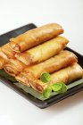 Closeup view of piled Spring rolls with herb on black plate — Stock Photo