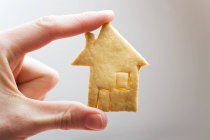 Closeup cropped view of hand holding house-shaped cookie — Stock Photo