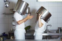 Two chefs having discussion with large pans on heads — Stock Photo