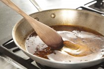 Vue rapprochée de la glaçure de grattage sur la casserole avec cuillère en bois — Photo de stock