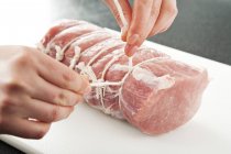 Mãos femininas amarrando carne de porco crua — Fotografia de Stock