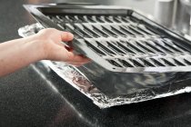 Primo piano vista di una mano che mette una padella per griglia su una padella foderata di alluminio — Foto stock