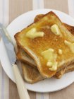 Closeup top view of buttered toasts with knife on plate — Stock Photo