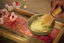 Vue rapprochée de la main mélangeant thé vert japonais Matcha dans un bol cérémonial avec fouet — Photo de stock