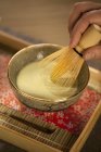 Vue rapprochée du mélange à la main de thé vert japonais Matcha dans un bol cérémonial avec fouet — Photo de stock