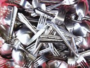 Closeup top view of cutlery heap with red reflections — Stock Photo