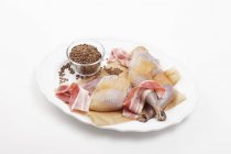 Ингредиенты для фазана, завернутого в бекон в белой тарелке на белом фоне — стоковое фото