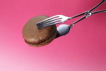 Cake tongs holding chocolate macaroon — Stock Photo