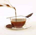 Vue rapprochée de verser le thé Rooibos infusé à tasse avec cuillère et chocolat — Photo de stock