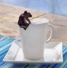 Closeup view of steamed milk in white mug with pear shaped chocolate stick — Stock Photo