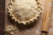 Closeup top view of formed raw pie and rolling pin — Stock Photo