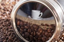 Cup and coffee beans heap reflected in metal tin surface — Stock Photo