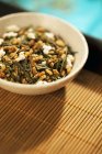 Vue rapprochée du mélange de thé vert en vrac Genmaicha dans un bol sur un plateau en bambou — Photo de stock