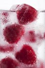 Glass of water with raspberry ice cubes — Stock Photo