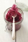 A jar of red cabbage salad with fork over wooden surface — Stock Photo