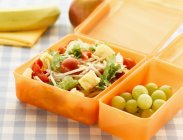 Vue rapprochée de la boîte à lunch avec salade et raisins — Photo de stock
