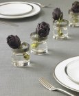 Ajuste de mesa con alcachofas en vasos de agua - foto de stock