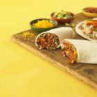 Veggie Burrito Reducido a la mitad con cuencos de relleno sobre escritorio de madera sobre superficie amarilla - foto de stock