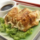 Closeup view of three potstickers with chopsticks and soy sauce — Stock Photo