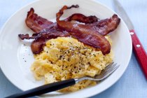 Closeup view of scrambled eggs and bacon on a white plate — Stock Photo