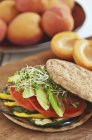 Sandwich végétarien à l'aubergine grillée, courgettes, poivrons jaunes, tomates et avocat sur un rouleau rond plat — Photo de stock