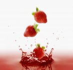Morangos caindo em suco vermelho — Fotografia de Stock