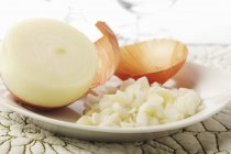 Cebolla blanca picada con media cebolla; Piel de cebolla en plato blanco - foto de stock