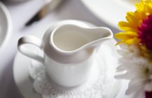Closeup view of white pitcher of ream and flowers — Stock Photo