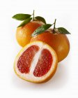 Красные грейпфруты с половинкой и листьями — стоковое фото