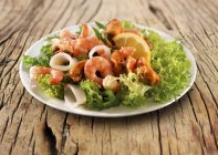Крупный план салата из морепродуктов с креветками и лимоном на тарелке — стоковое фото