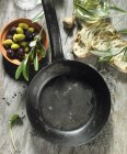 Una sartén vacía, salvia, aceitunas negras y verdes, aceite de oliva, una ramita de oliva, ciabatta de oliva y lavanda - foto de stock