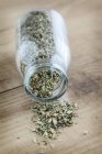 Closeup view of herbal mix in overturned glass bottle and on wooden surface — Stock Photo
