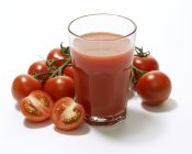 Glass of tomato juice surrounded by tomatoes — Stock Photo