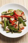 Remover-frito cubos de tofu y verduras sarna tout, calabacín y pimientos rojos con salsa de soja en plato blanco - foto de stock