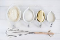 Top view of baking ingredients with whisk on white surface — Stock Photo
