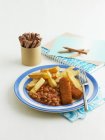 Fischstäbchen mit gebackenen Bohnen und Chips auf blauem Teller über weißer Oberfläche — Stockfoto