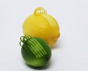 Lemon and lime with curling zest — Stock Photo