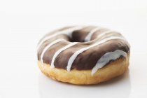 Closeup view of one chocolate glazed donut on white surface — Stock Photo