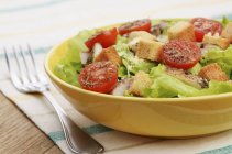 Mixed leaf salad with chicken, tomatoes and croutons in yellow plate over tbale with fork — Stock Photo